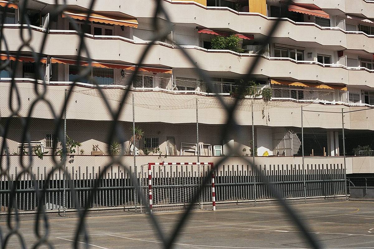 Fachada de un bloque de viviendas tras una valla metálica.