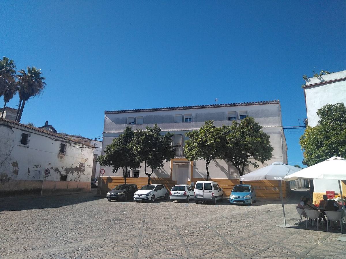 Edificio de viviendas en una plaza con zona de aparcamiento.